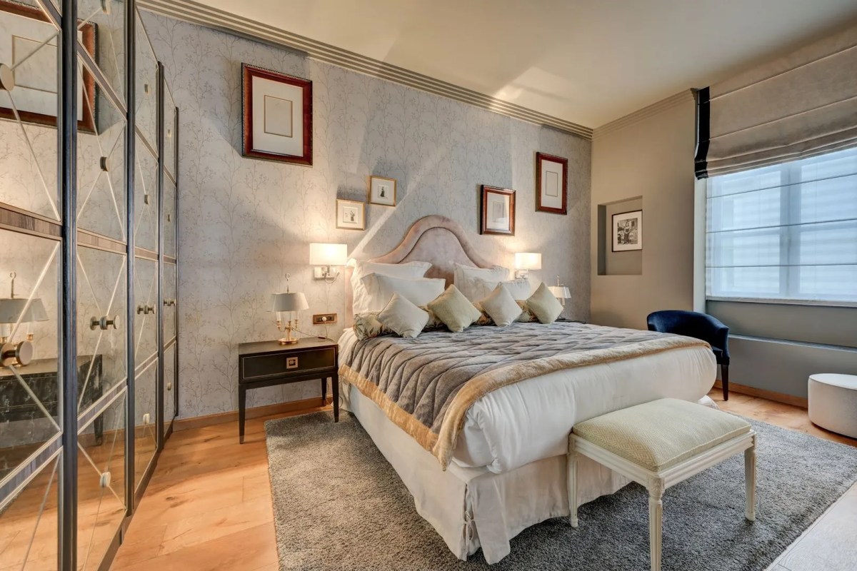 Elegant hotel bedroom with grey tufted headboard, artwork, and mirrored wardrobe