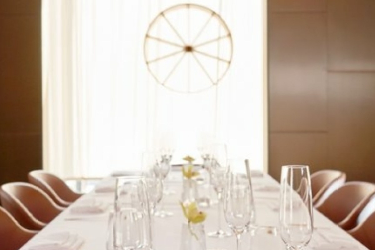 Elegant private dining room with long table set with glassware, white linens, and circular wheel-like light fixture