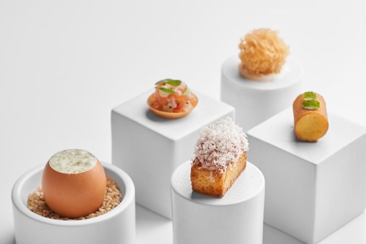 Artfully plated bite-sized dishes displayed on white pedestals, including an egg shell dish and canapés