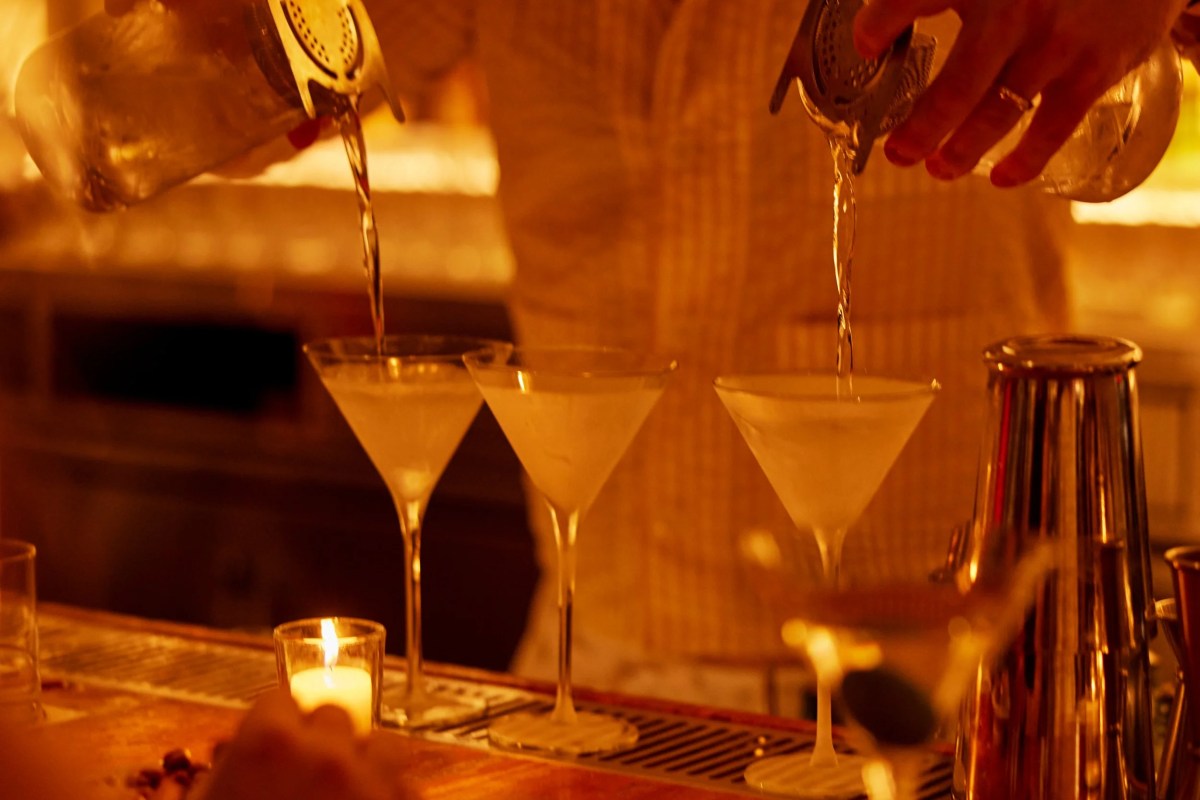 Bartender pouring martinis into glasses at a warmly lit bar