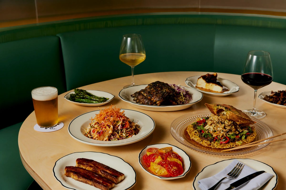 Round table in a green booth set with multiple dishes, wine and beer glasses