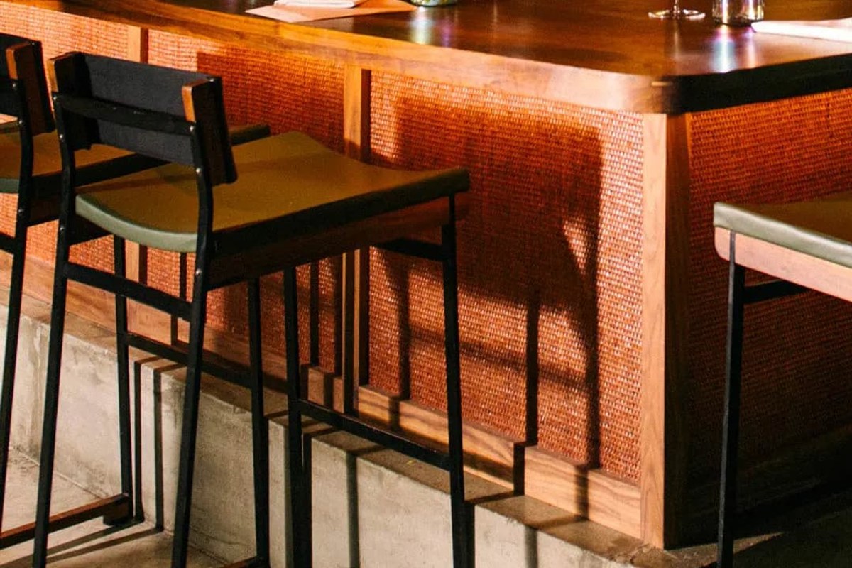 Close-up of wooden bar counter with woven rattan paneling and black bar stools