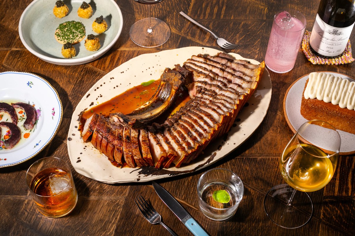 Wooden table spread with sliced pork, caviar bites, cake, cocktails and wine