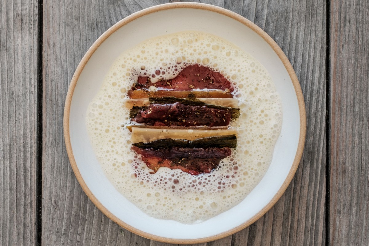 Plated dish with foam sauce and three striped slices of meat/vegetable on a ceramic plate on a wooden table