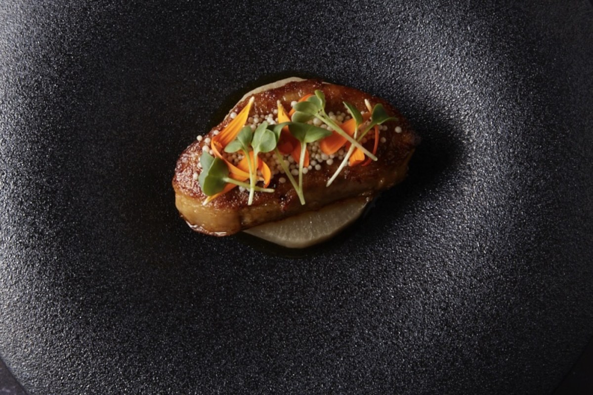 Artfully plated dish of seared foie gras with edible flowers and microgreens on dark plate