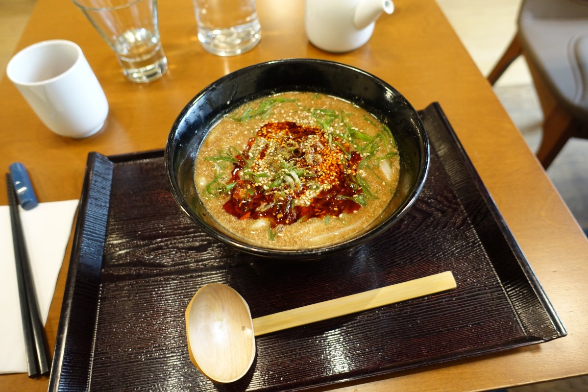 Overhead view of a bowl of tantanmen udon with soup, served on a tray with chopsticks and a wooden spoon