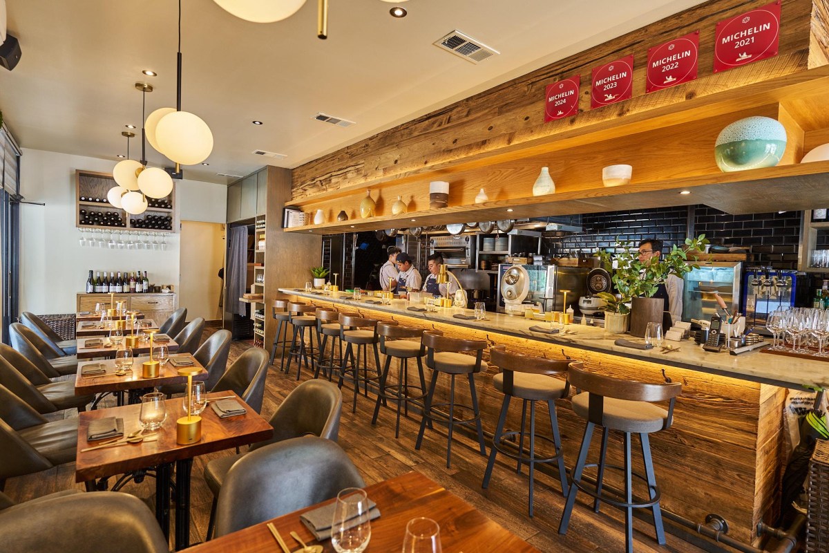Interior of Kochi restaurant showing bar seating, dining tables, and open kitchen with Michelin plaques displayed