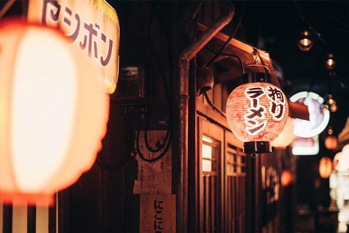 Red paper lantern reading 'Kodawari Ramen' hanging outside the restaurant at night, neon signs in alley