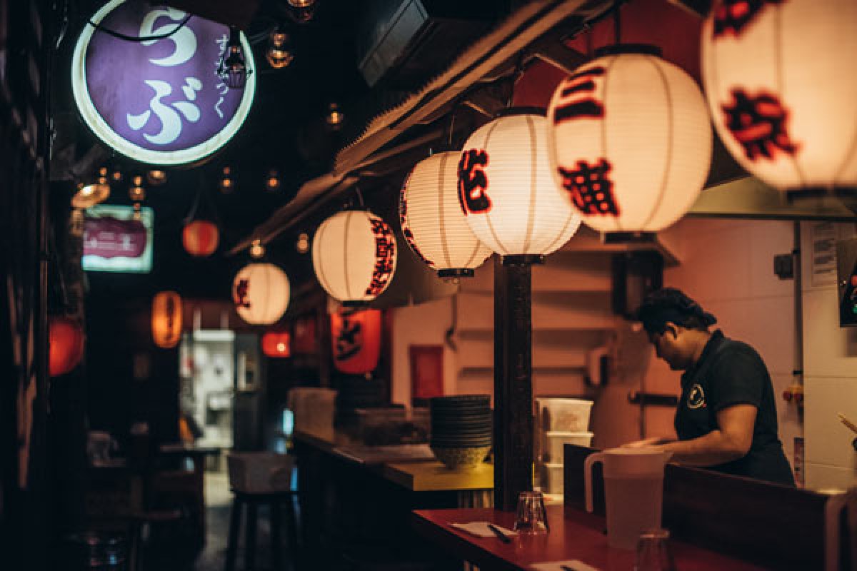 Restaurant interior with red counter, bar stools, hanging paper lanterns, and staff member working behind counter