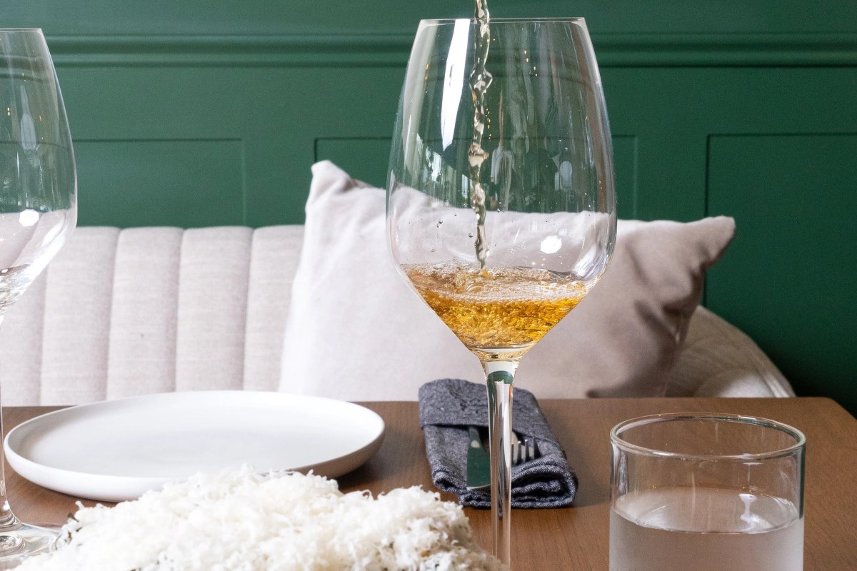 Wine being poured into a glass at a table set with white plate and napkin against green wall