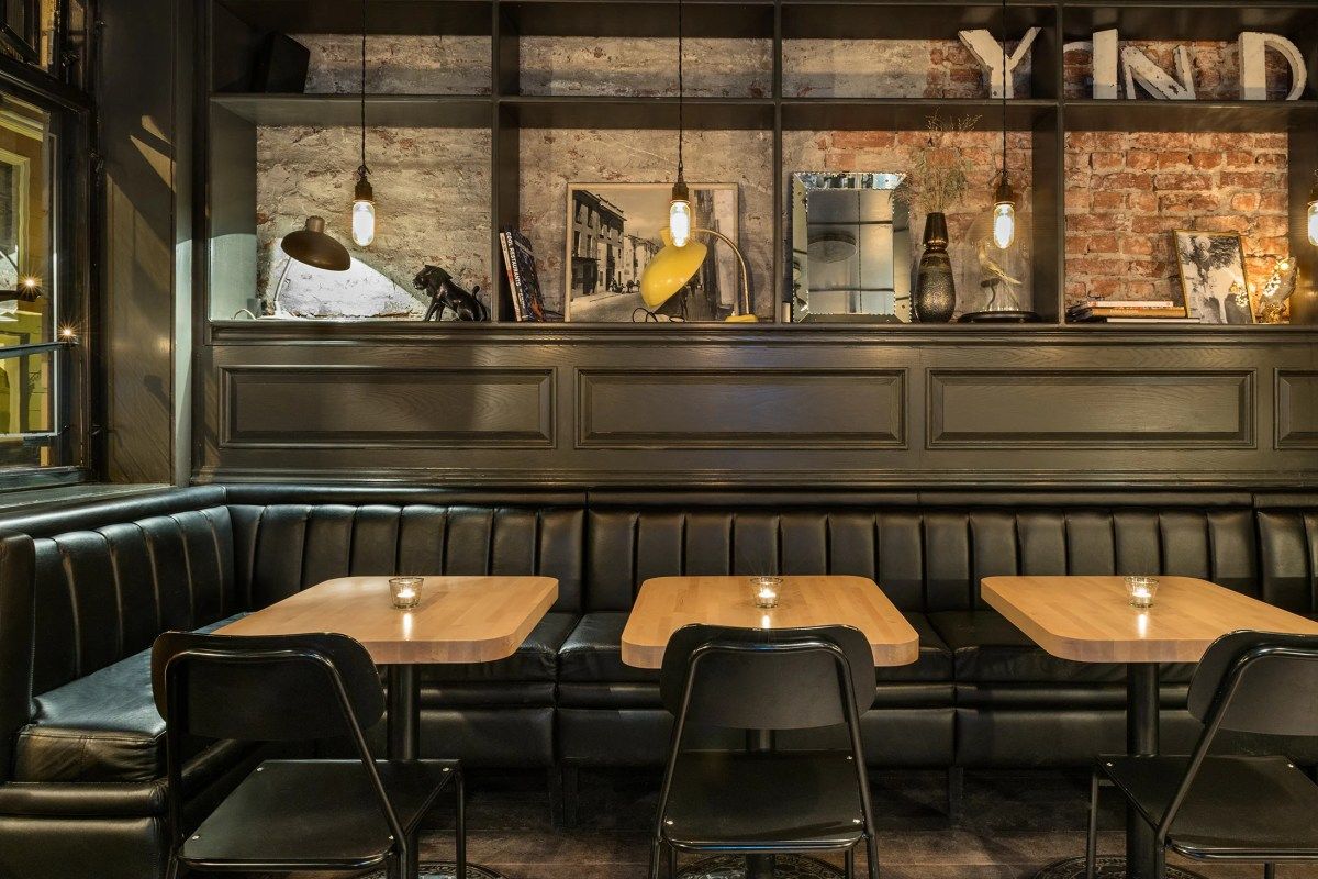 Restaurant dining area with booth seating, wooden tables, exposed brick and shelving with decor
