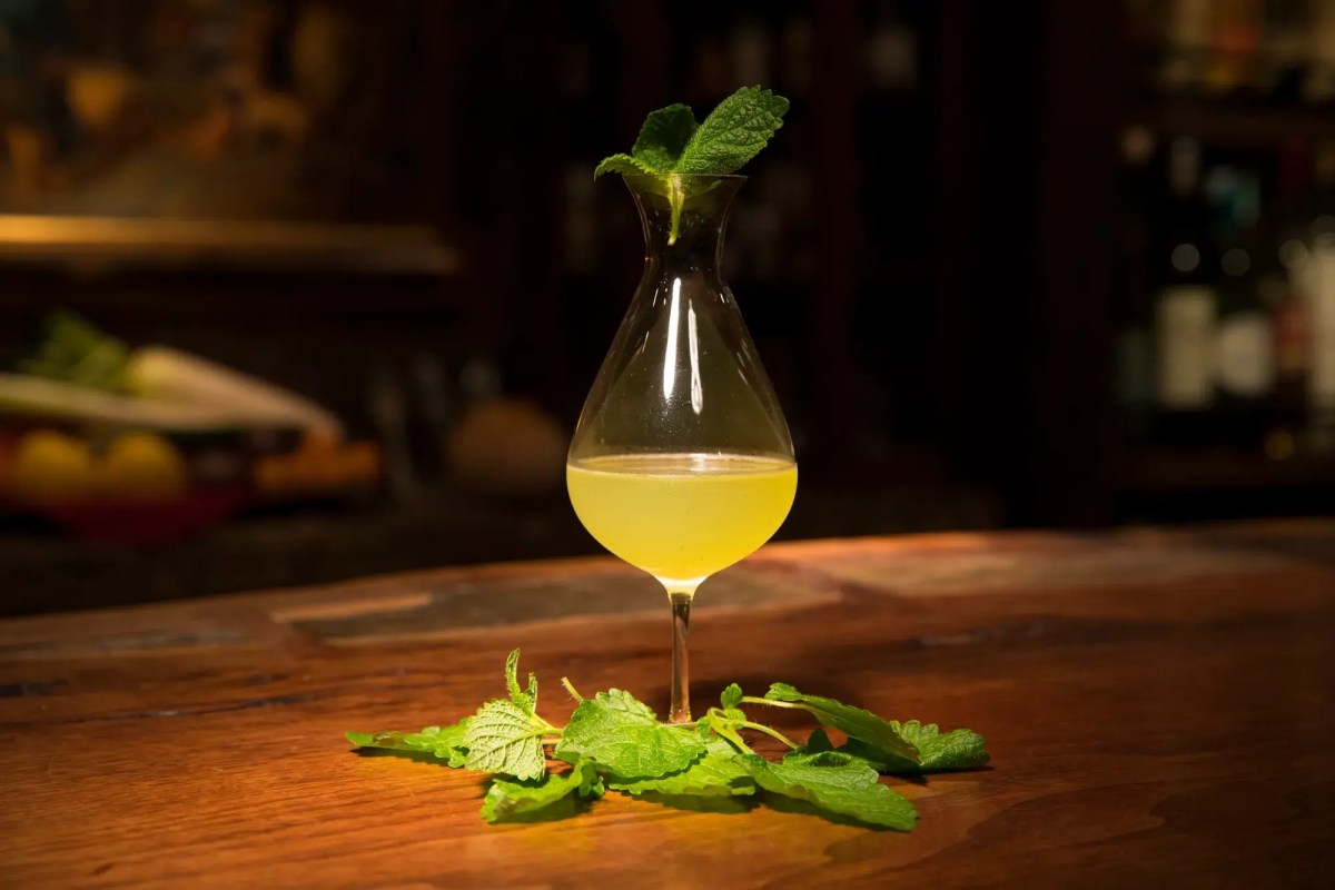 Close-up of a yellow cocktail in a carafe-style glass garnished with mint on a wooden bar