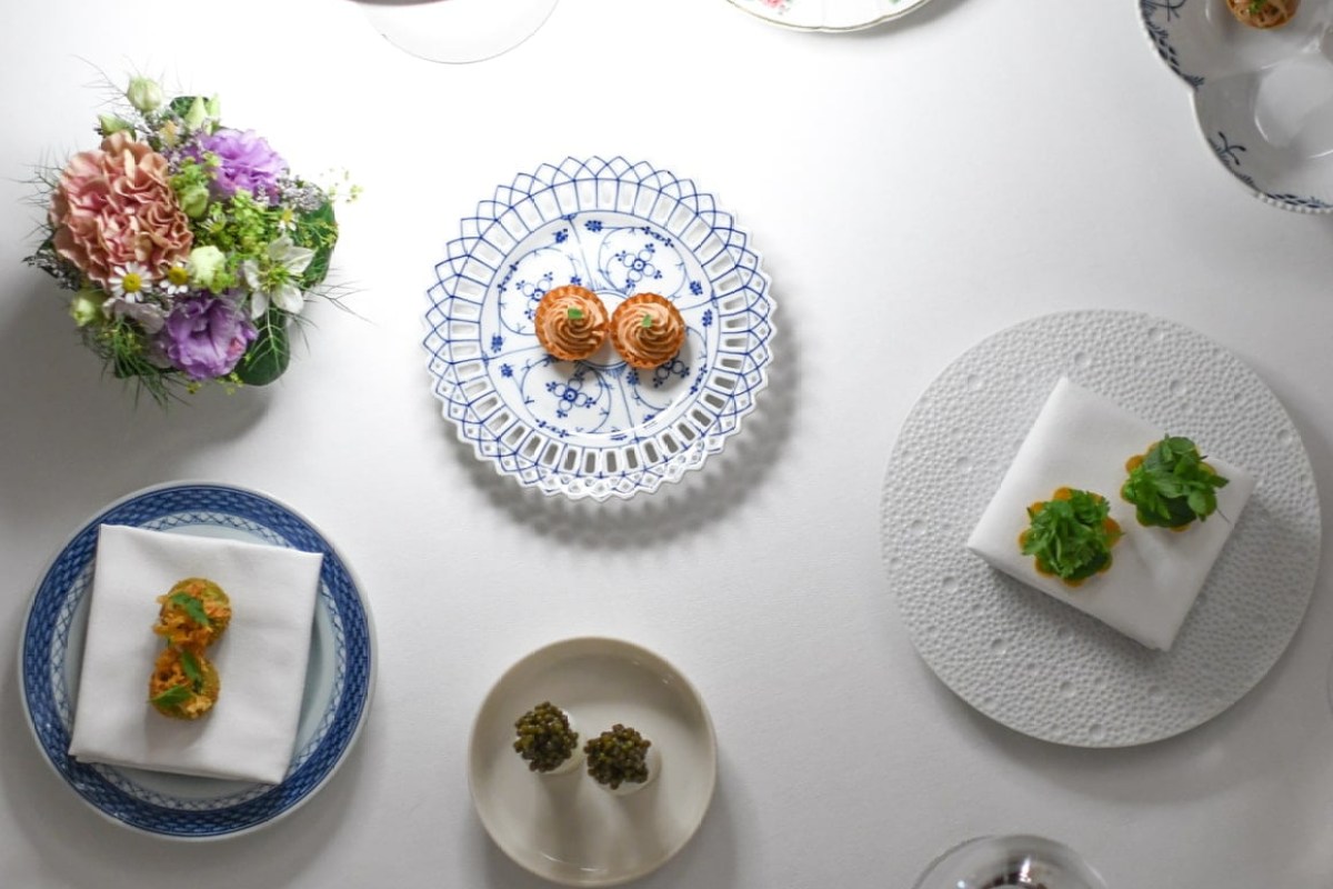 Overhead flat-lay of several small tasting dishes, flowers and patterned plates on a white tablecloth at Kong Hans Kælder