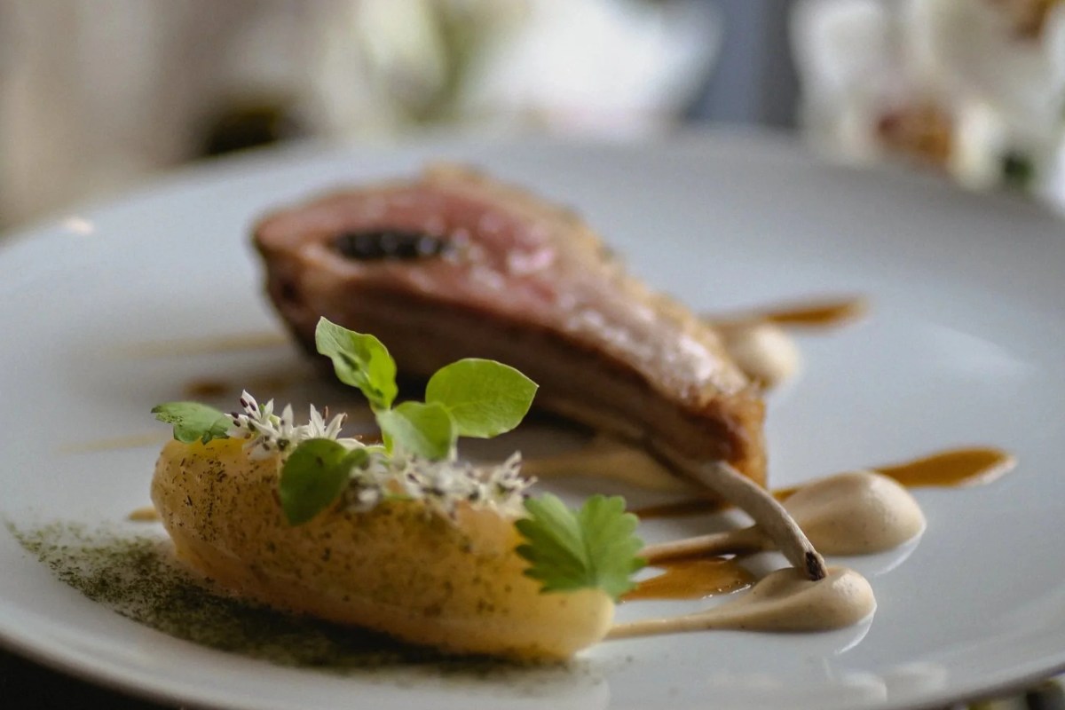 Plated meat dish with seared cutlet, caviar, pear puree and herb garnish on white plate.