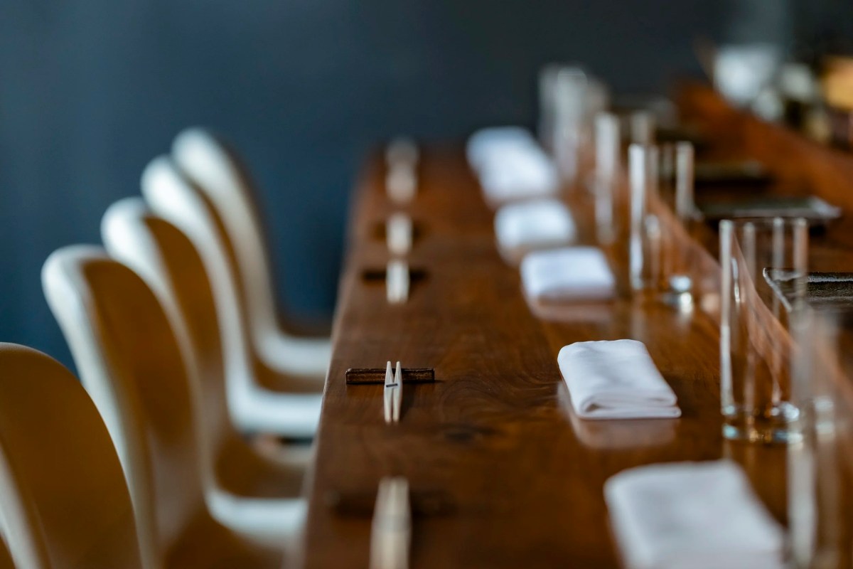 Long wooden counter set with folded white napkins, chopsticks, and glassware in a dim dining room