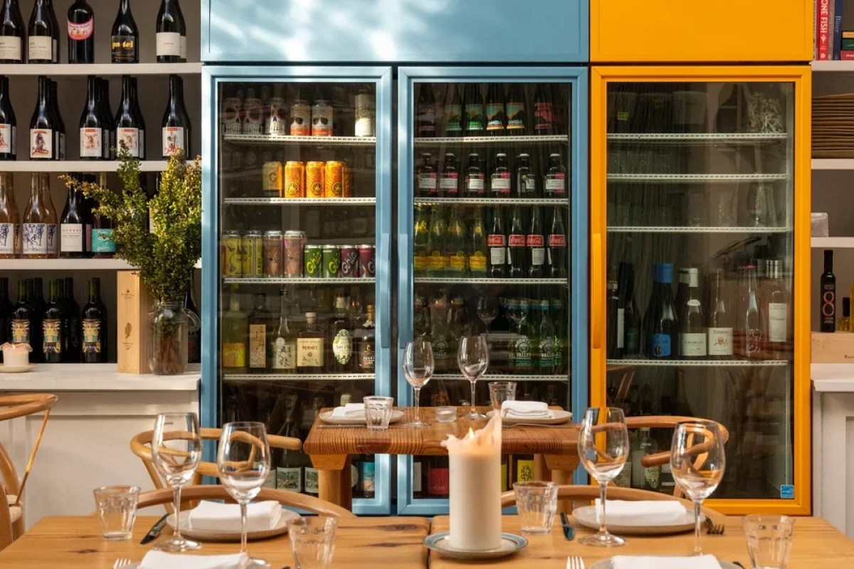 Restaurant dining room with colorful glass-front beverage coolers, wine shelves, and a set wooden table