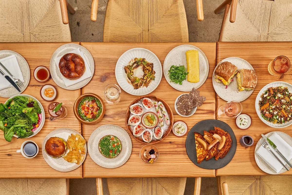 Overhead view of a wooden table filled with a variety of dishes including oysters, salads, sandwiches, and burgers