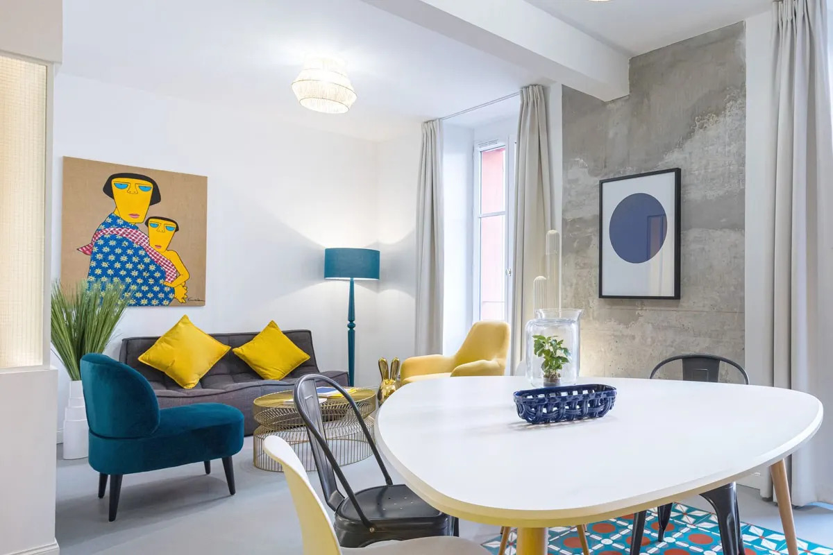 Colorful guest living room with artwork, teal and yellow armchairs, dining table