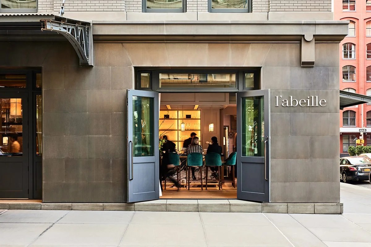 Exterior entrance of L'Abeille restaurant with open doors showing dining room and bar seating