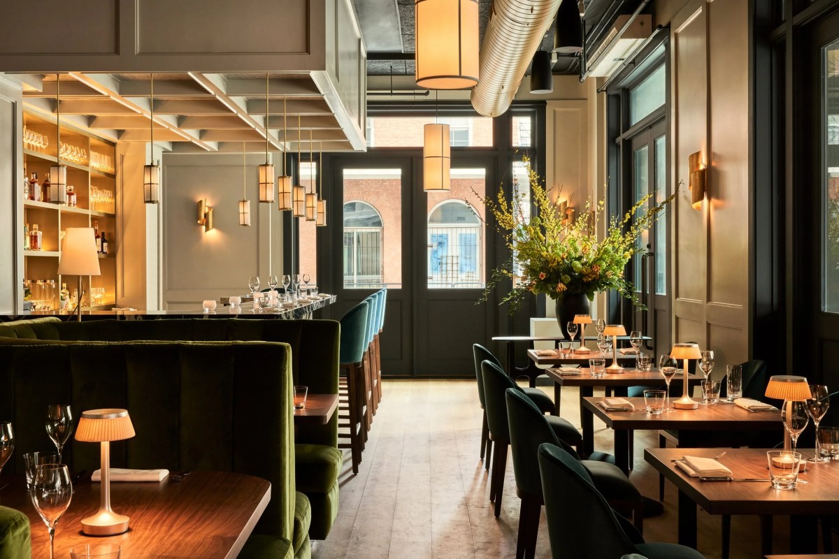 Elegant dining room with green velvet booths, bar, brass pendant lights and floral arrangement