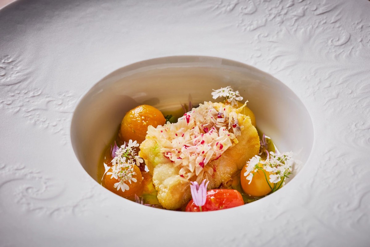 Plated dish with fried fish, citrus segments, edible flowers in a white sculpted bowl