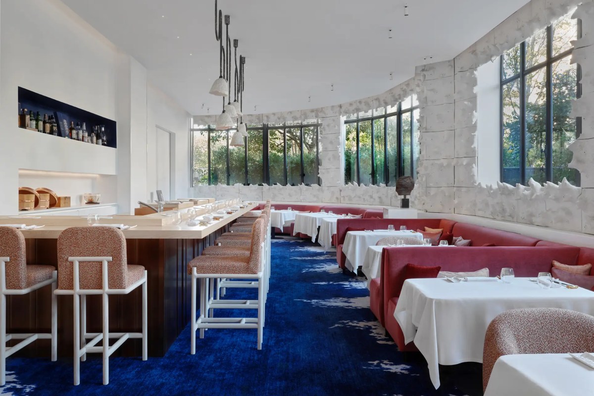 Elegant dining room with red velvet banquettes, blue carpet, bar counter, and large windows overlooking greenery
