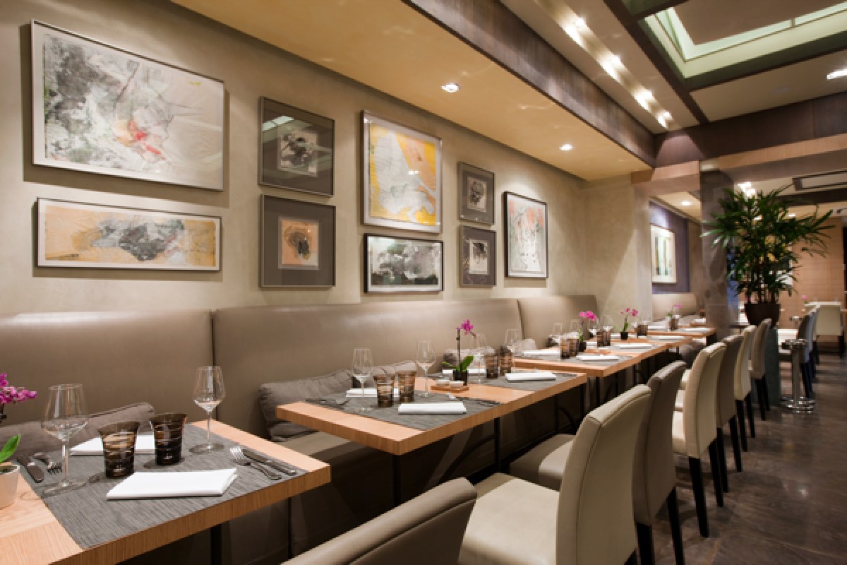 Close view of restaurant dining area with banquette seating, modern abstract art on wall, and set tables