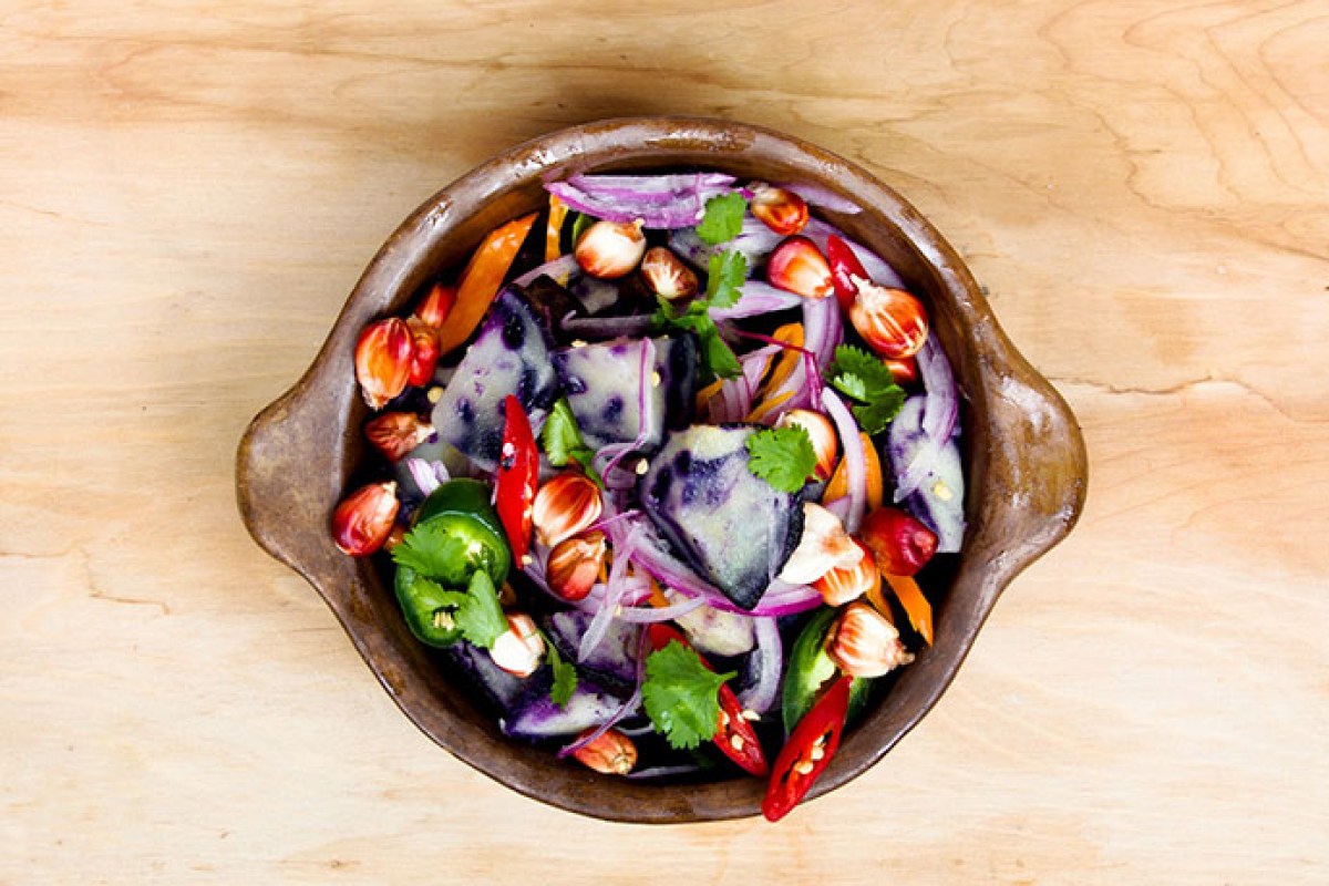 Overhead shot of a rustic bowl holding a colorful salad with purple potatoes, red onion, chili peppers and cilantro