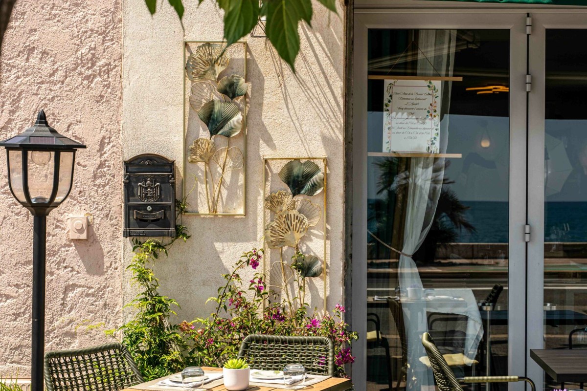 Restaurant exterior terrace with outdoor tables, decorative wall art, and glass doors reflecting the sea