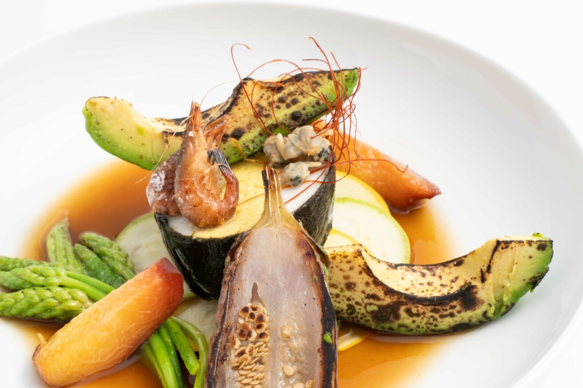 Plated dish of grilled vegetables, shrimp, and seafood in a light broth on a white plate