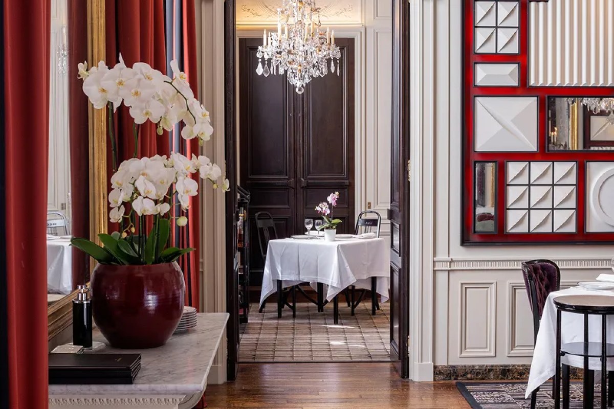 Elegant dining room interior with orchid, chandelier through doorway, and framed red/white decorative panel