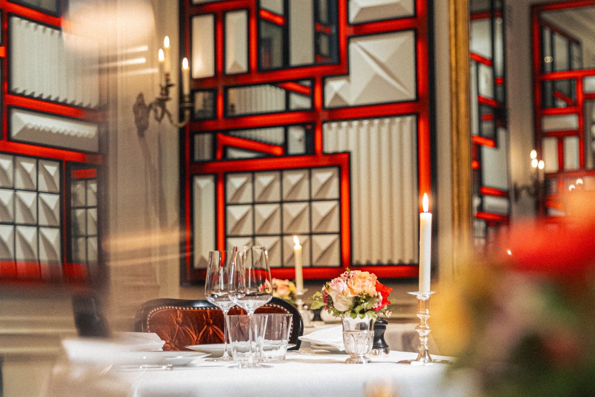 Candlelit table setting with wine glasses and flowers in front of a red geometric mirrored wall panel