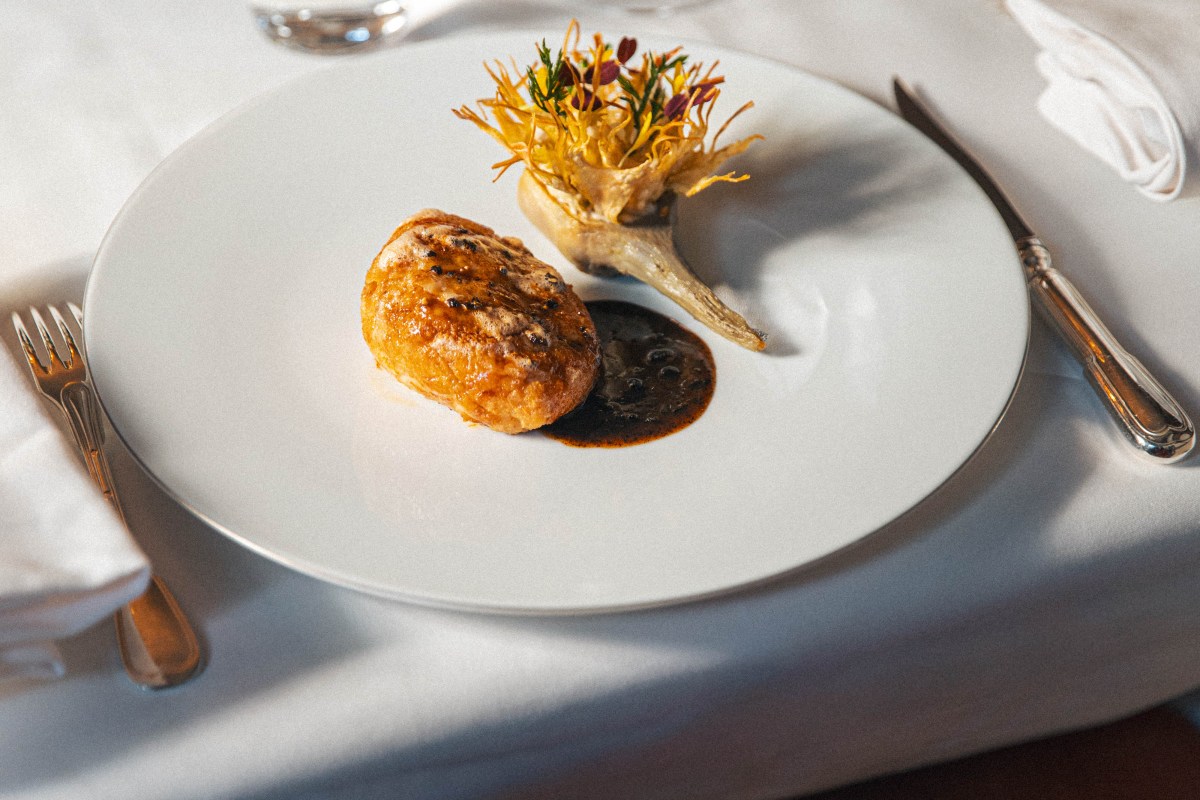 Plated foie gras dish with pastry crust, dark sauce and crispy garnish on white plate