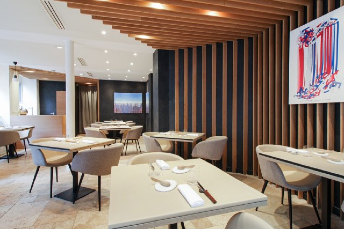 Spacious dining room with wood slat ceiling, dark wall, multiple set tables, chairs, and framed city artwork