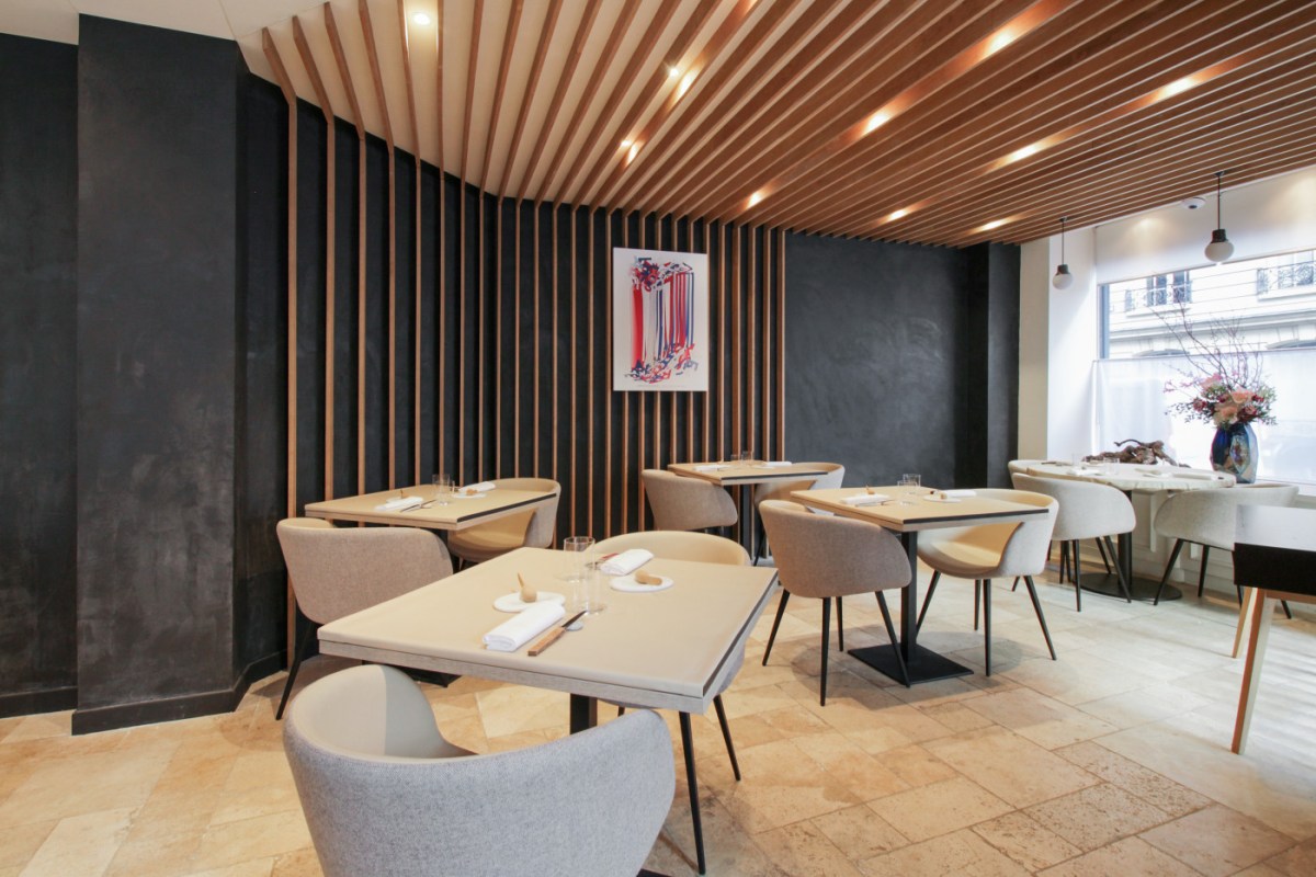 Dining room with wood slat ceiling and wall, set tables, colorful artwork, window with flower arrangement