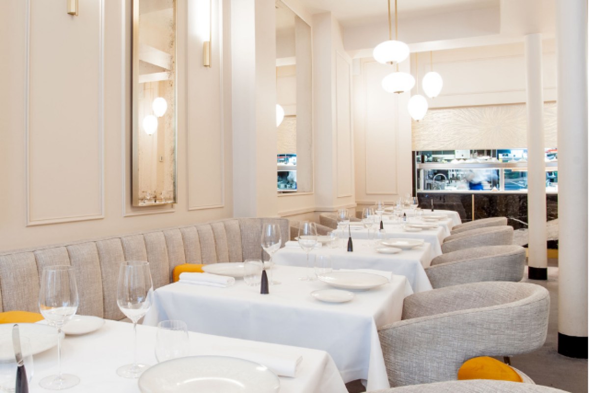 Restaurant dining room view showing open kitchen pass and white table settings