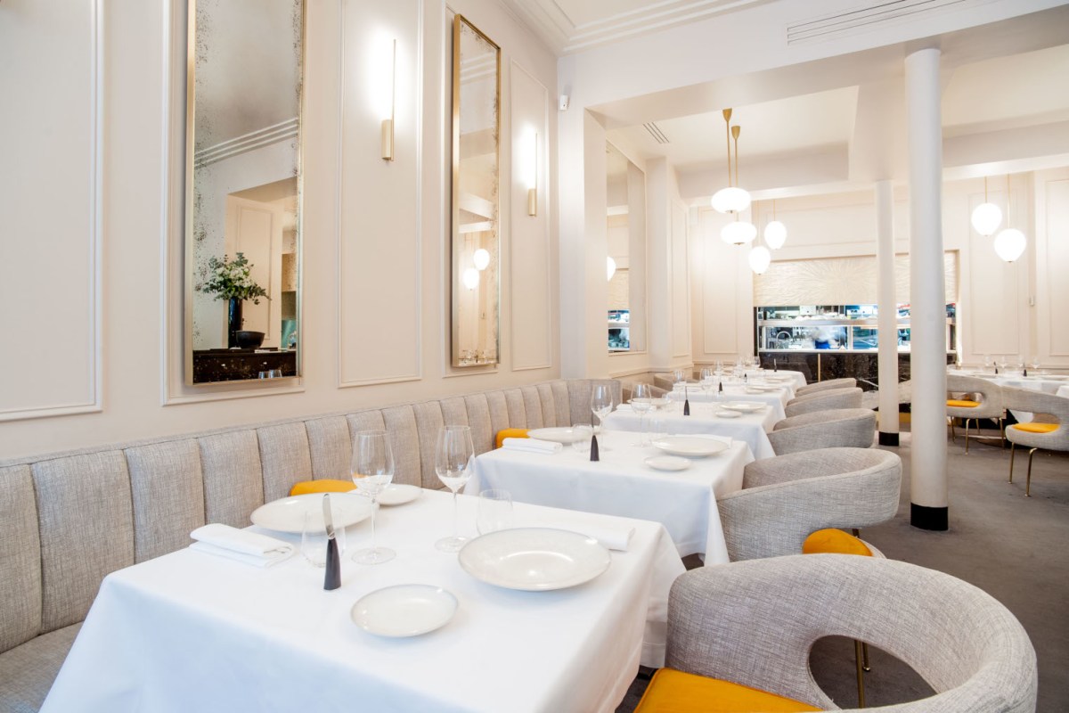Elegant dining room with white-clothed tables, grey banquette seating and mirrored walls