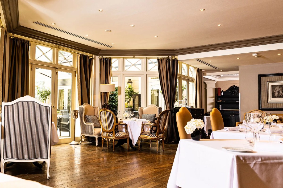 Elegant dining room with white-clothed tables, striped armchairs and large windows leading to terrace