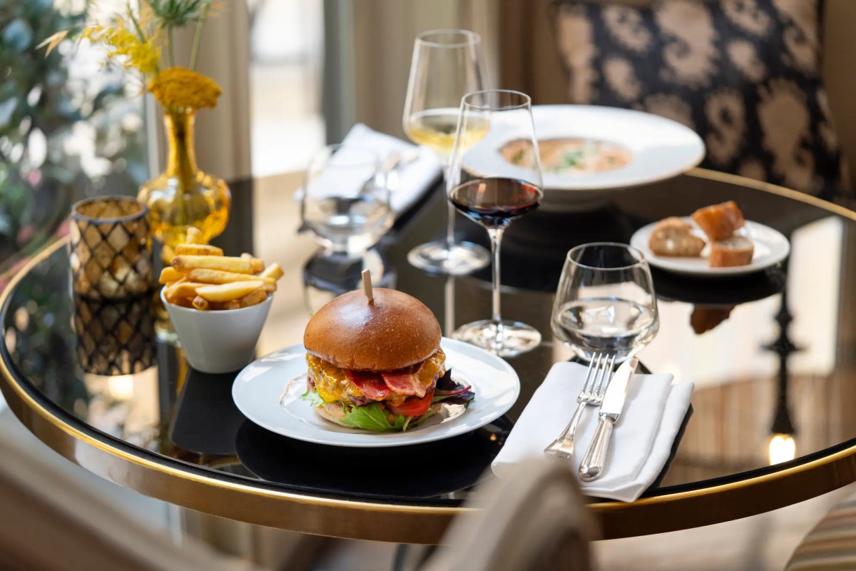 Laid table with burger, fries, wine glasses and bread on a glass table