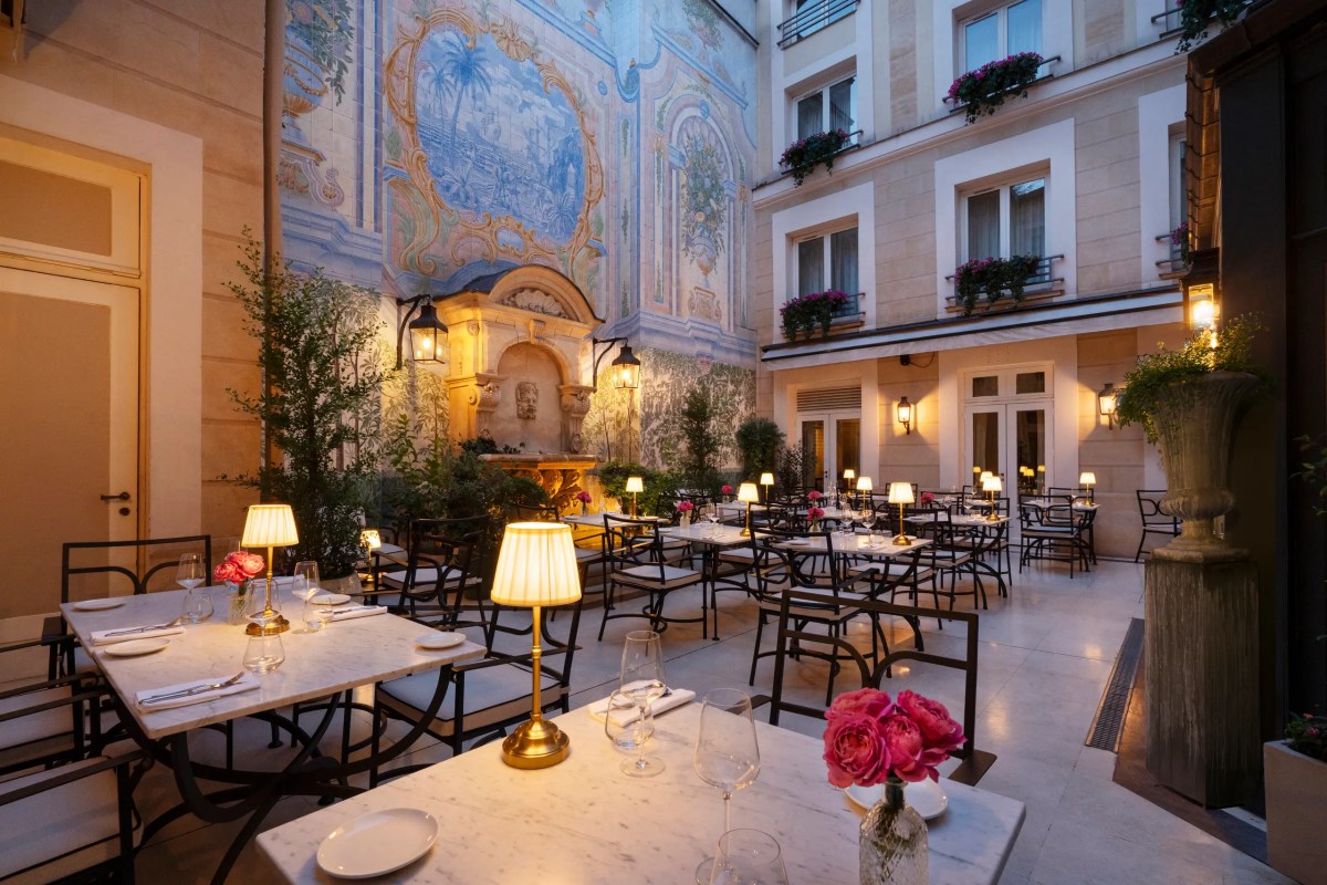 Frescoed inner courtyard of L'Assaggio at dusk, with lamp-lit tables set around a stone fountain