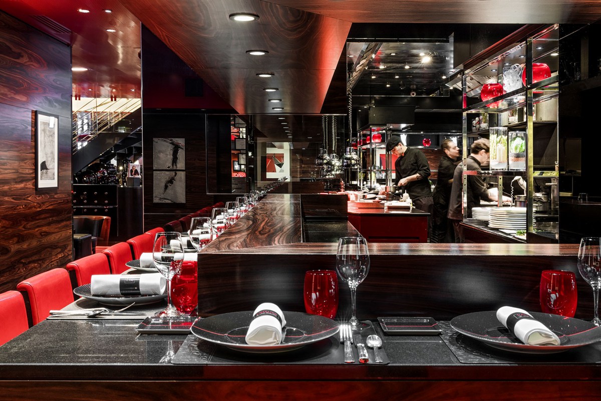 Dining room with red leather banquettes, dark wood bar counter, and open kitchen with chefs visible