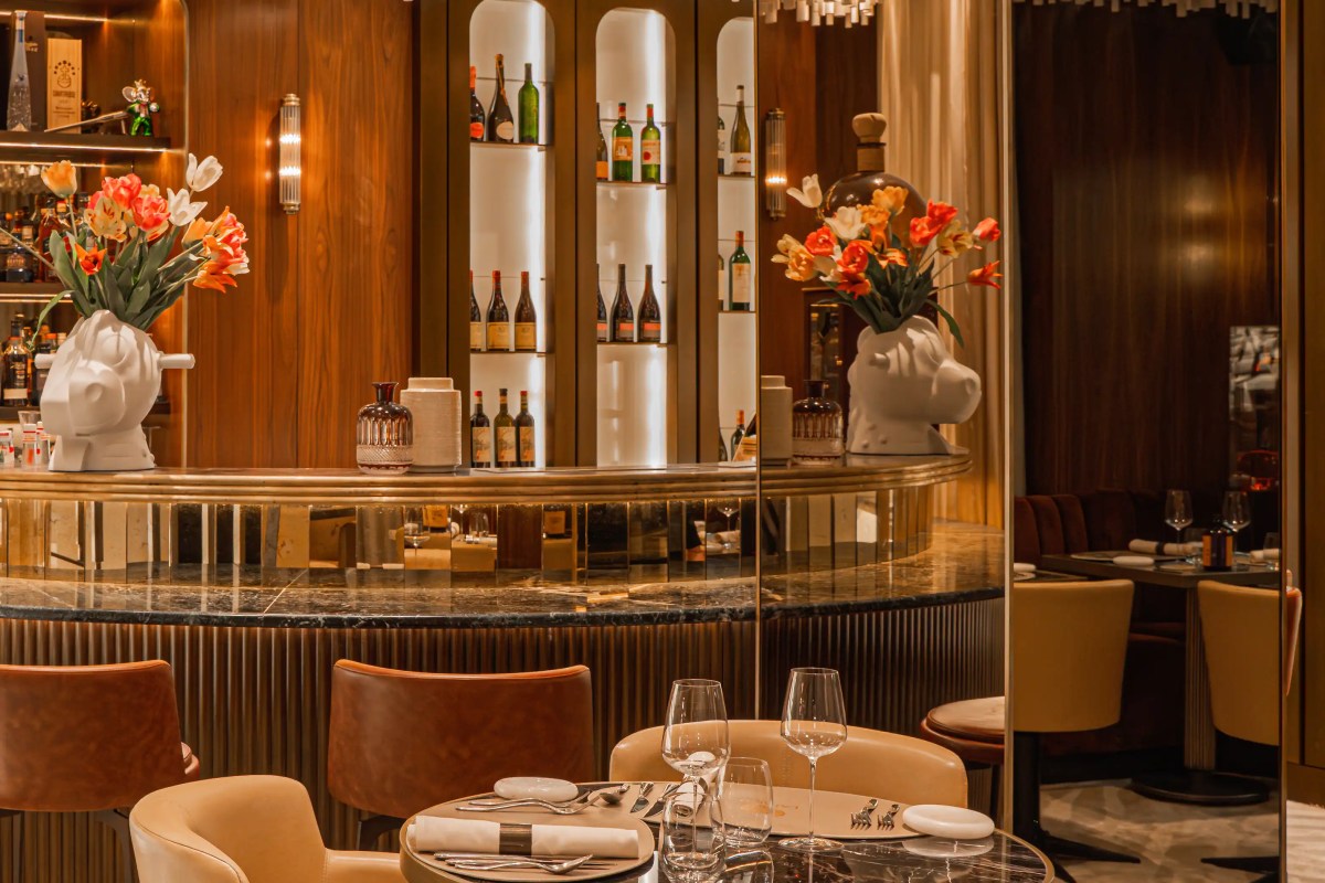 Elegant bar and dining area with marble counter, bottles on shelves, flowers, and a table set with wine glasses and silverware