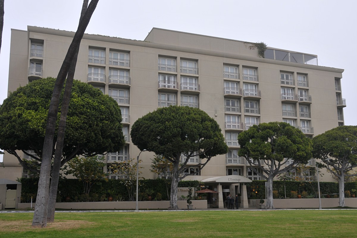 Exterior facade of L'Ermitage Beverly Hills hotel with balconies, trees, and entrance visible, under overcast sky