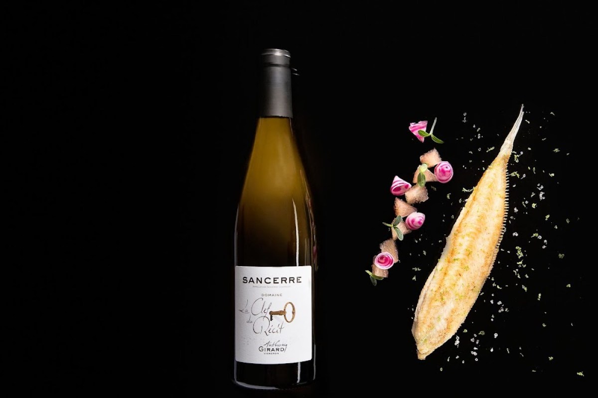 Bottle of Sancerre wine beside a plated fish dish garnished with pink flowers and herbs on a black background