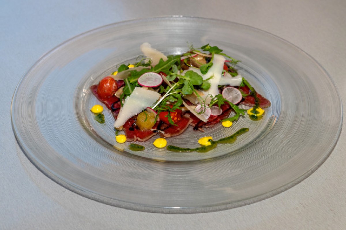 Elegant plated beef carpaccio with arugula, parmesan shavings, radish and sauces on glass plate