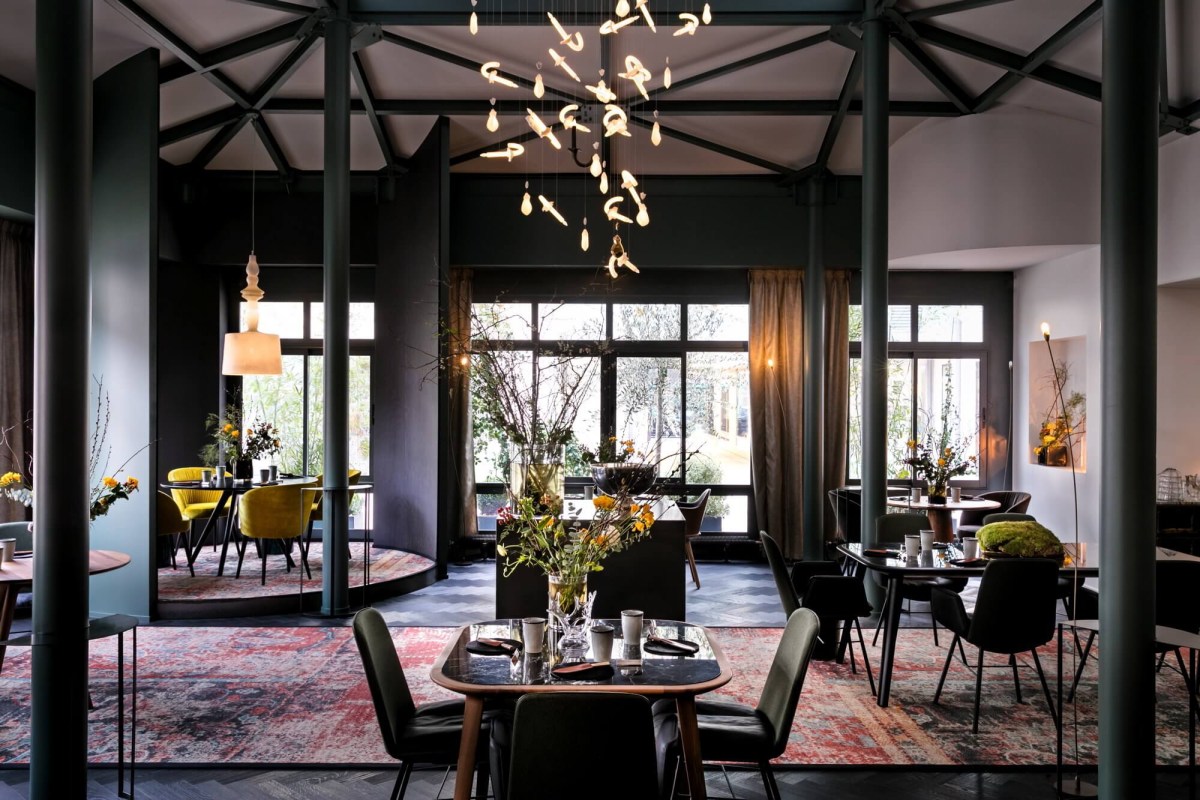 Elegant dining room interior with patterned rug, dark round tables, hanging sculptural light fixture and large windows