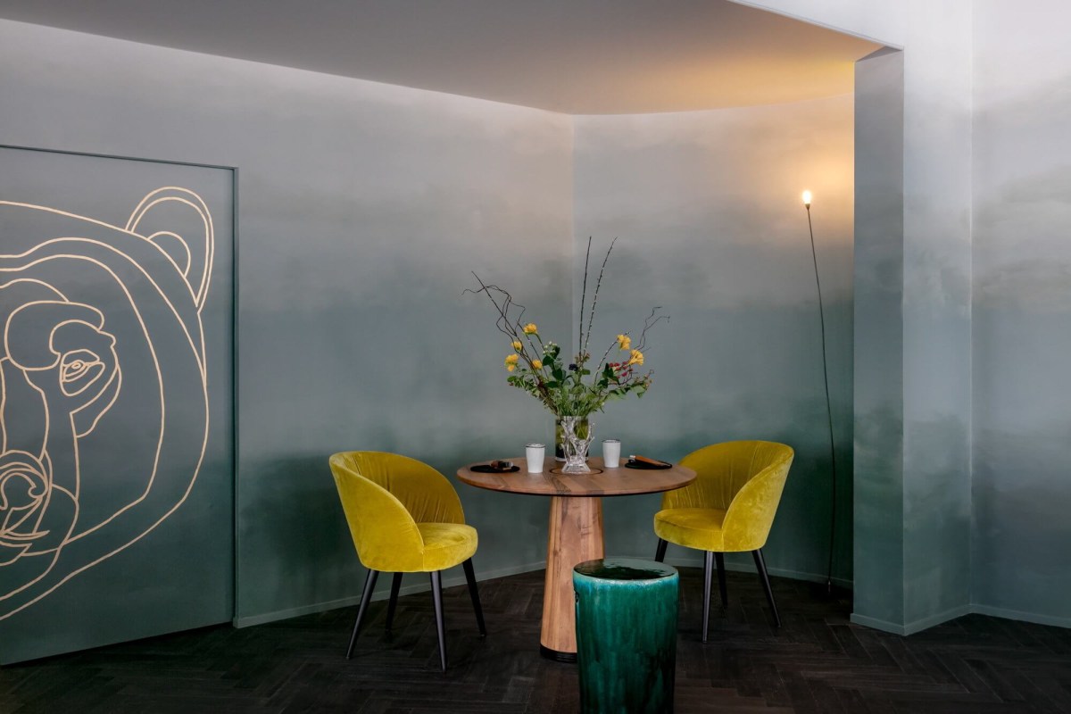 Cozy corner nook with two mustard-yellow velvet chairs around a small round table under a bear mural wall