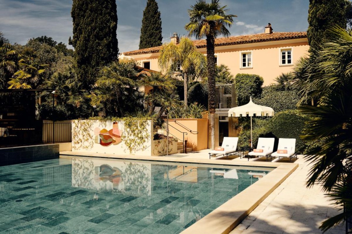 Pool and terrace area with loungers, backed by the hotel's peach façade and gardens
