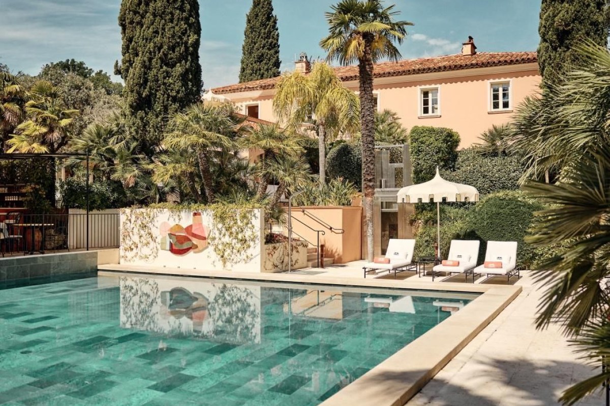 Pool with loungers in front of the peach-colored hotel building, palm trees surrounding