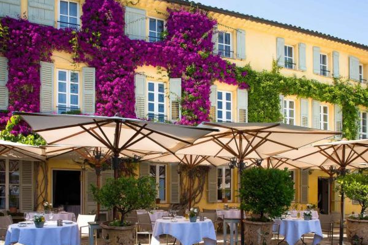 Restaurant facade covered in vivid purple bougainvillea, terrace with umbrellas and set tables below